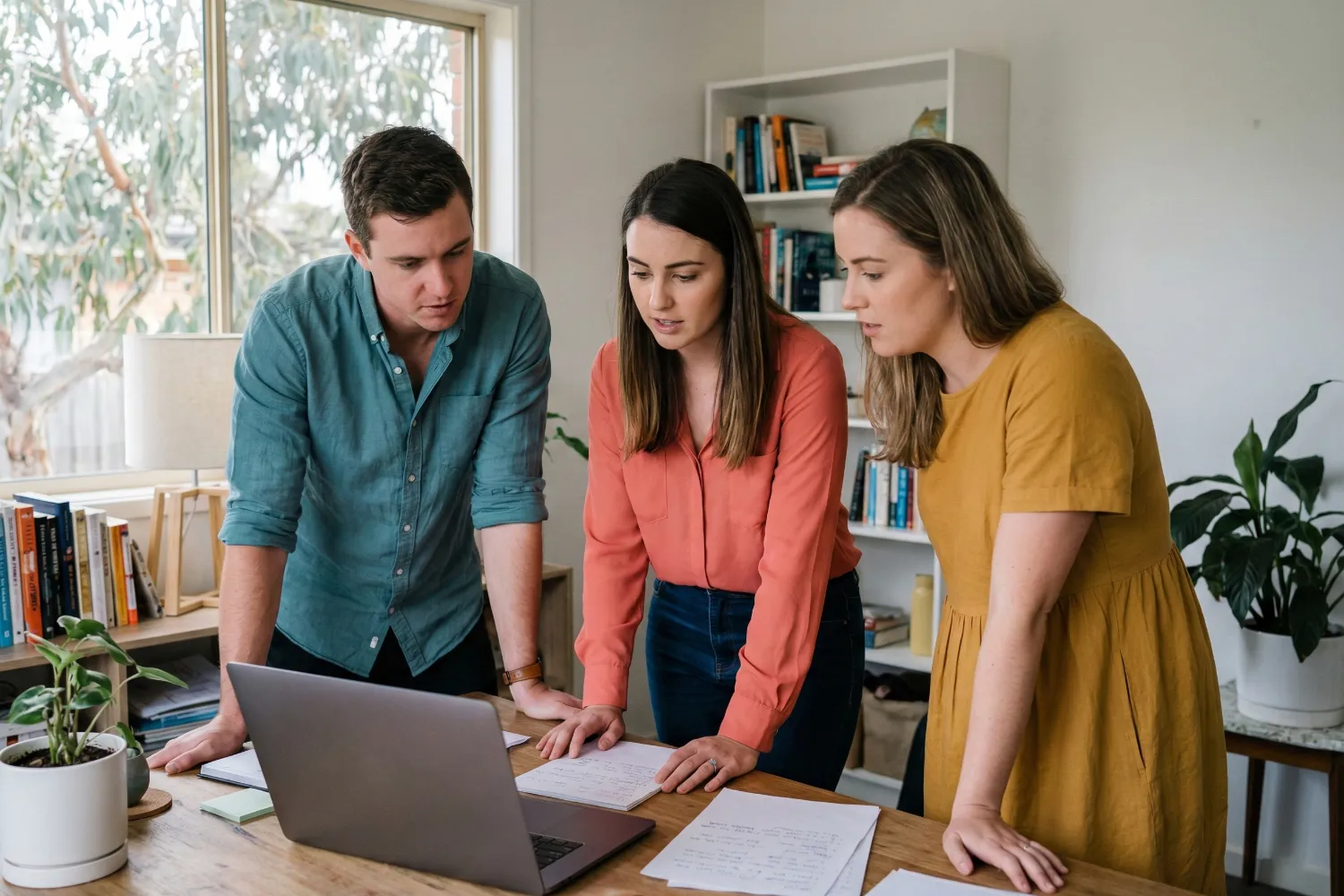 Young Australian entrepreneurs working together in a modest home garage workspace. They appear to collaborate over business ideas with laptops and notes.